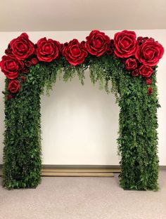 red roses and greenery are arranged in an arch