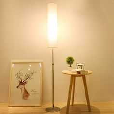 a lamp next to a table with a picture on it and a plant in the corner