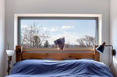 a bed sitting under a window next to a wooden headboard and night stand with a blue blanket on it