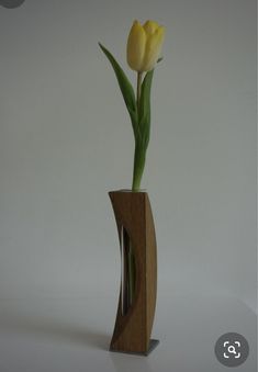 a yellow flower in a wooden vase on a white surface with an inscription below it