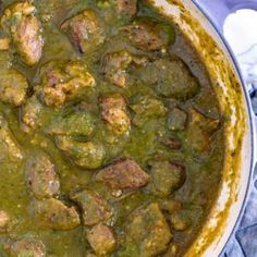 a large pot filled with meat and green sauce on top of a blue table cloth