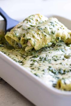 a white casserole dish filled with spinach and chicken enchiladas