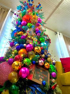 a brightly colored christmas tree with ornaments and decorations on it's top, in a living room