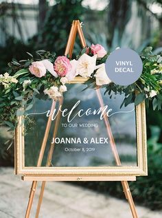 a welcome sign with flowers and greenery is displayed in front of a wooden easel