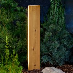 a tall wooden object sitting in the middle of a garden next to some bushes and trees