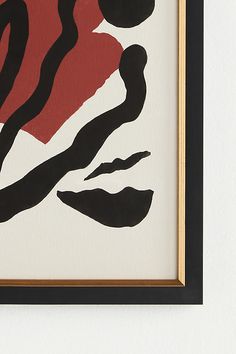 an abstract painting with black and red colors in a gold frame on a white wall