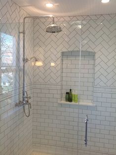 a white tiled bathroom with glass shower doors and shelves on the wall next to it