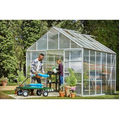 a man and woman standing in front of a green house with lawn mowers