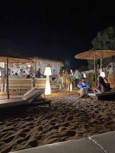 people sitting on the beach at night with umbrellas and lounge chairs in the sand