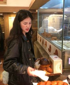 a woman standing in front of a display case filled with donuts