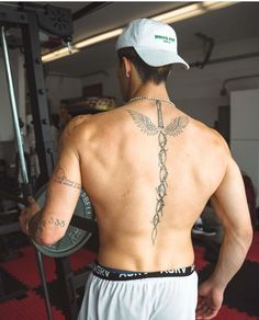 a man with a cross tattoo on his back is standing in front of a barbell