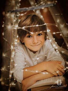 a young boy is smiling while sitting in front of a christmas tree with lights on it