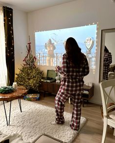 a woman in plaid pajamas is standing near a christmas tree