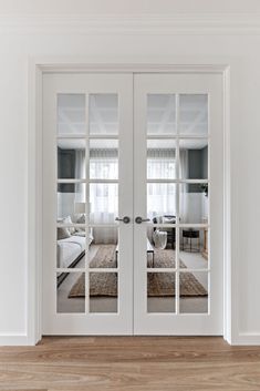 two white double doors with mirrors on them in a room that has hardwood floors and walls