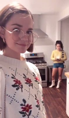 a woman wearing glasses standing in a kitchen next to another woman with her hand on her hip