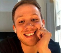 a young man smiles while holding his hand to his face and looking at the camera