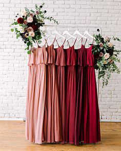 four bridesmaid dresses hanging up against a brick wall