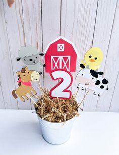 a cup filled with hay and farm animals on top of a white table next to a barn