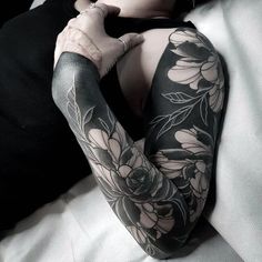 a woman laying on top of a bed covered in black and white tattoos with flowers