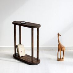 a small wooden giraffe standing next to a table with a book on it