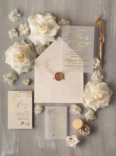 the wedding stationery is laid out with white flowers and gold foil lettering on it