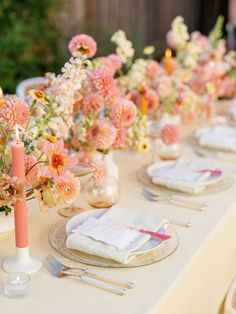 the table is set with pink and white flowers in vases, napkins, and silverware