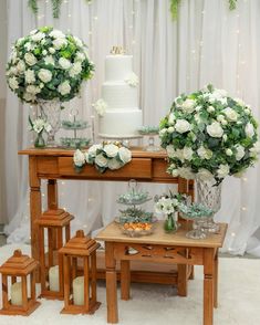 a table topped with white flowers and greenery next to a cake on top of a wooden table