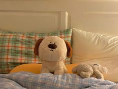 a stuffed dog sitting on top of a bed next to another stuffed animal and pillows