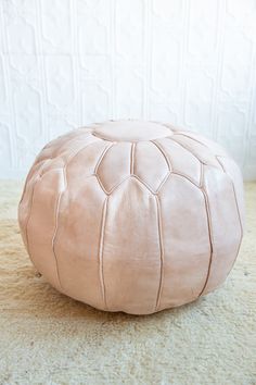 a pink leather poufle sitting on top of a carpeted floor next to a white wall