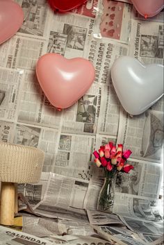 there are many heart shaped balloons hanging on the wall next to a vase with flowers