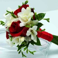 a red and white bridal bouquet on a clear glass vase with water in the background