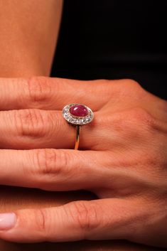 a woman's hand holding a ring with a red stone in the middle and white diamonds around it