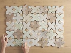 a person is placing tile on top of a wooden table to make a wall decoration