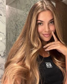 a woman with long blonde hair posing for a photo in front of a marble wall