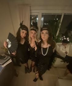 three women dressed up in flappers and garb, posing for the camera with one holding a fan