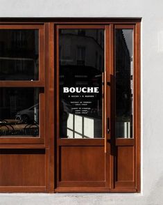 an open wooden door on the side of a white building with glass panels and french doors