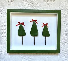 three small green trees are in a shadow box with red ribbon on them and tied to the sides