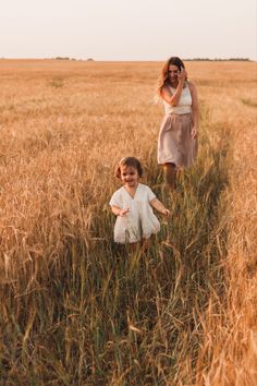 a woman and child are walking through tall grass in the middle of an open field