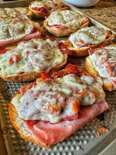 several sandwiches with meat and cheese are on a baking sheet, ready to be eaten