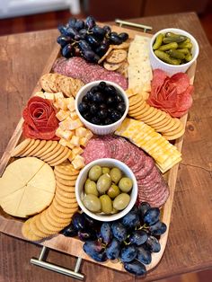 an assortment of cheeses, crackers and olives on a wooden platter