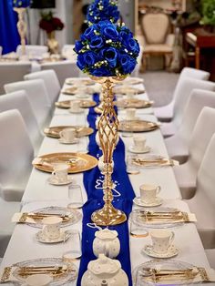 a long table set with blue flowers and gold place settings for formal dinnereons