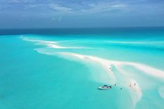 an aerial view of people walking on the white sand beach and boat in the water