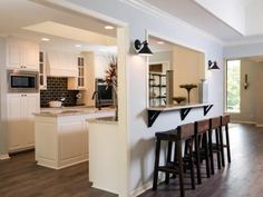 an open kitchen and living room area with bar stools in the center, along with hardwood flooring