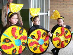 three children in costumes holding up large plates with lemon slices on them, and one child wearing