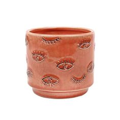 an orange ceramic cup with eyeballs and eyelashes painted on it's sides, in front of a white background