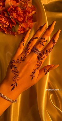 a woman's hand with henna tattoos on it and flowers in the background