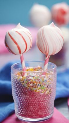 two candy lollipops sitting on top of a cup filled with sprinkles