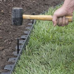 a man is holding a hammer and digging in the ground with some grass behind him