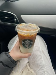 a person holding up a cup of coffee in their hand while sitting in a car