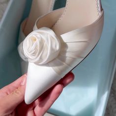 a person is holding a white shoe with a flower on the heel and it's pointed toe